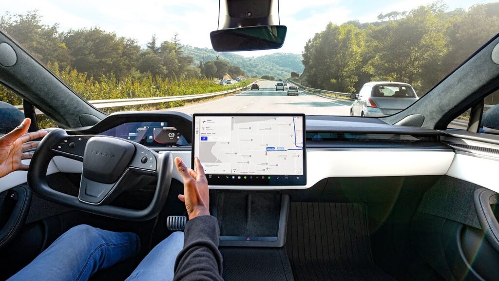 Self-driving car interior with steering wheel and touch screen display showing navigation on a highway.