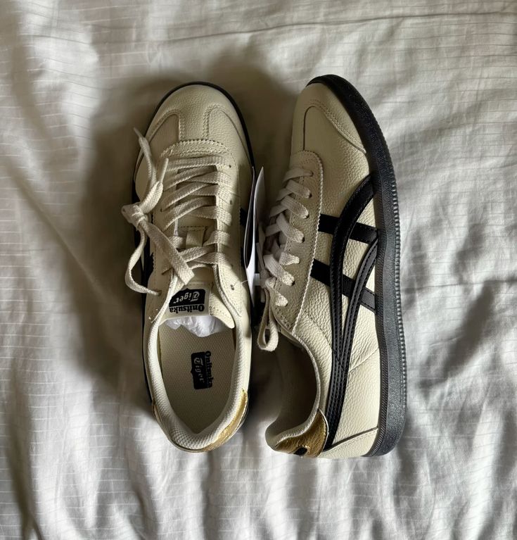 Cream Onitsuka Tiger sneakers with black stripes on a white bedsheet, showcasing stylish design and comfort.