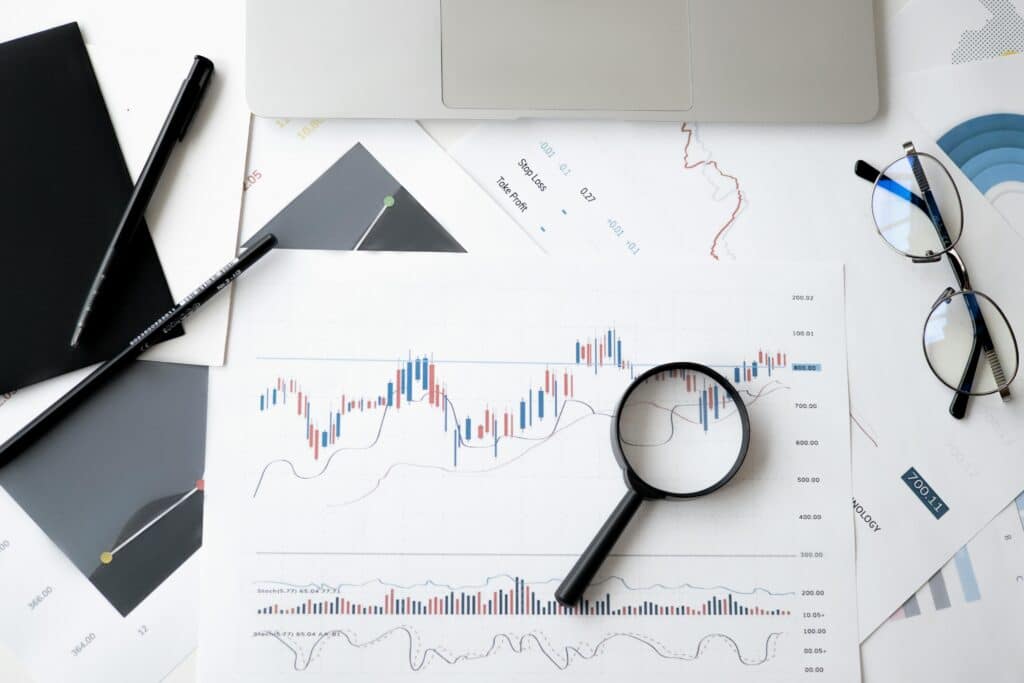 Magnifying glass on stock market charts with glasses and a laptop. Analyzing financial data and market trends.