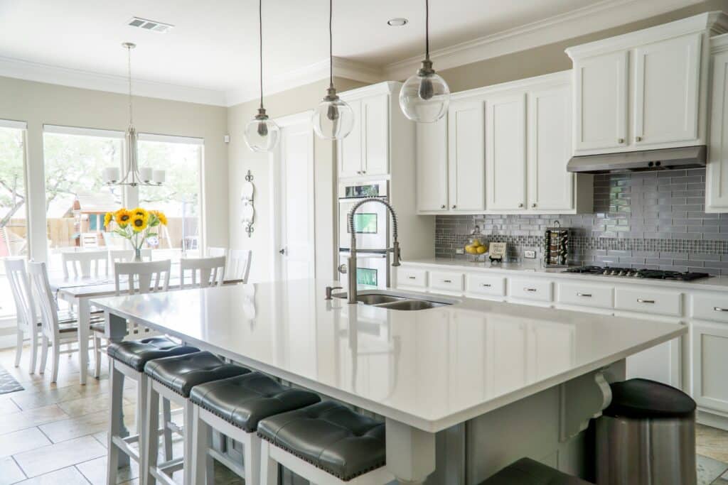 Bright kitchen with white cabinets, large island, pendant lights, and sunflowers on the dining table.