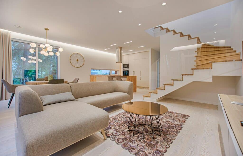 Modern living room with beige sofa, round coffee table, stylish chandelier, and floating staircase.