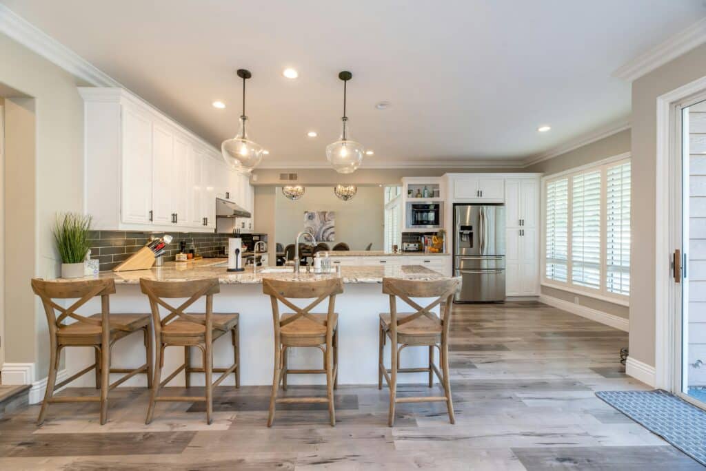 Modern kitchen with island, three wooden stools, pendant lighting, and stainless steel appliances.