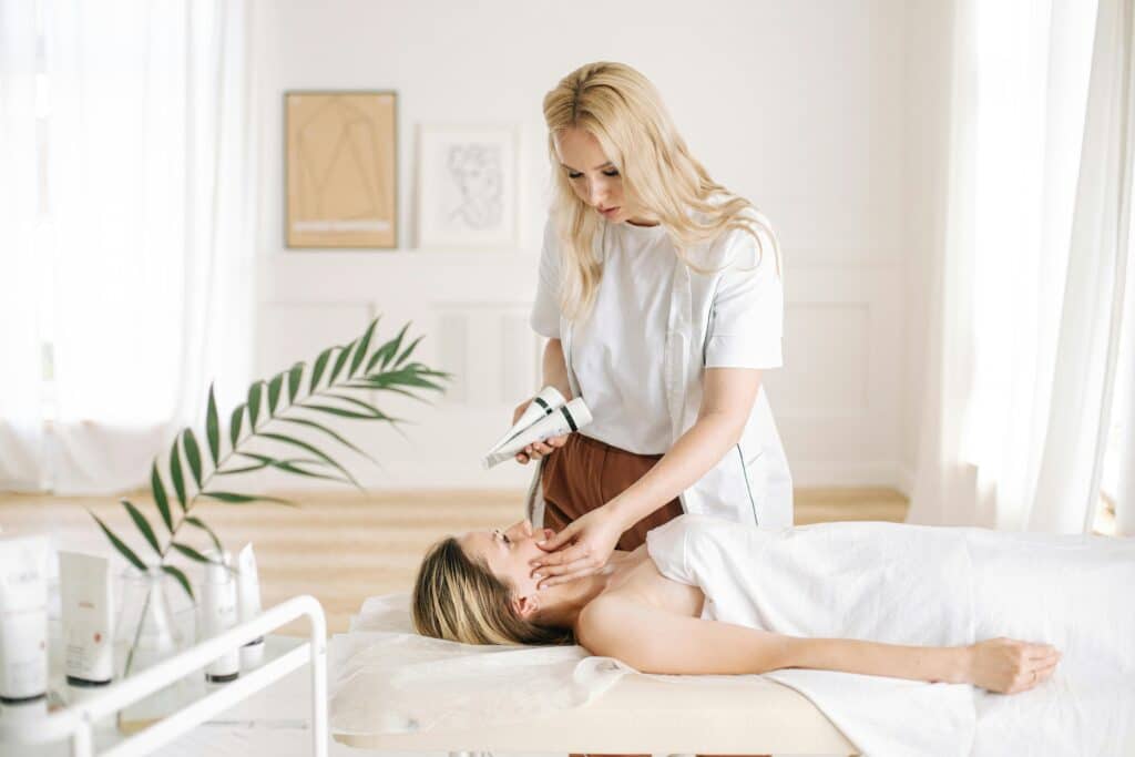 Woman receiving a relaxing facial treatment in a spa setting with skincare products nearby.