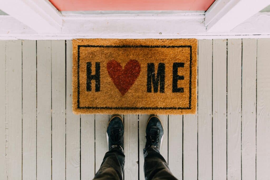 pexels-kelly-2950003 Welcome mat with HOME and a heart shape on a wooden porch, viewed from above with feet in black shoes. | Sky Rye Design Welcome mat with HOME and a heart shape on a wooden porch, viewed from above with feet in black shoes.