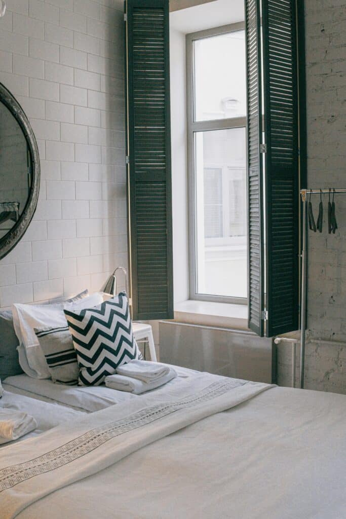 Cozy bedroom with chevron pillow, large window, and wall mirror for a modern minimalist design.