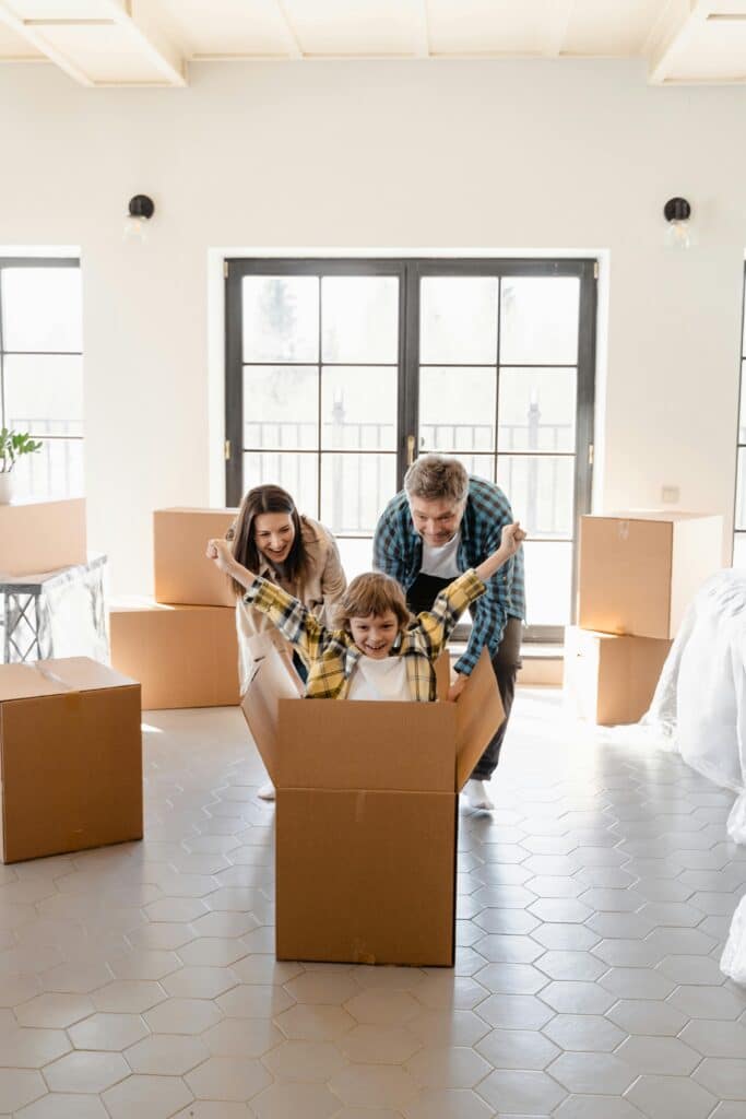 Family joyfully playing with cardboard boxes in a sunlit room during a move.