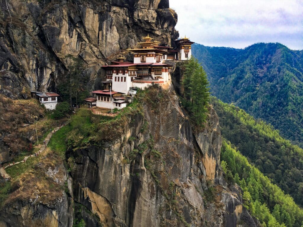 Cliffside monastery perched on a rocky mountain in Bhutan surrounded by lush green forest and rugged terrain.