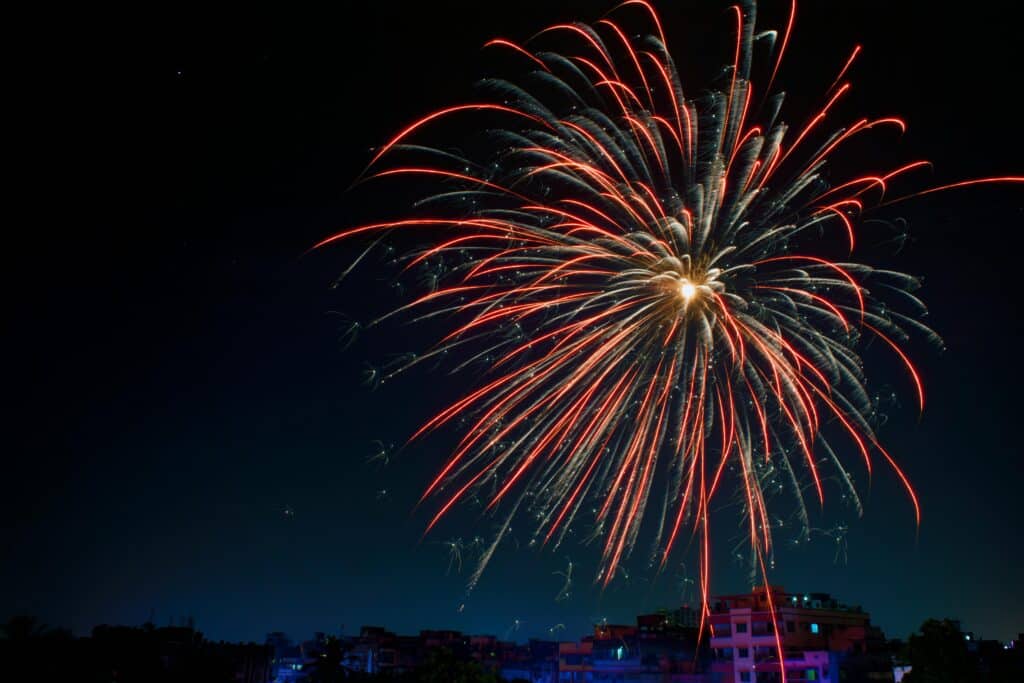 Vibrant red fireworks bursting in the night sky above a cityscape.