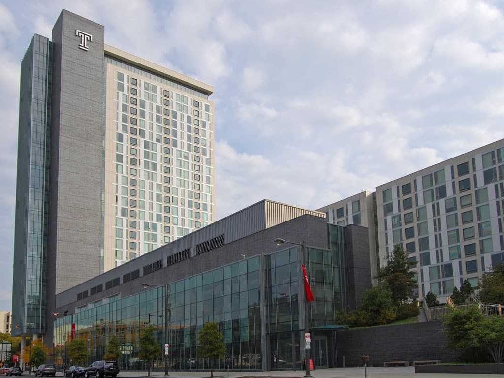 Modern university campus building with glass facade and a tall tower on a clear day.