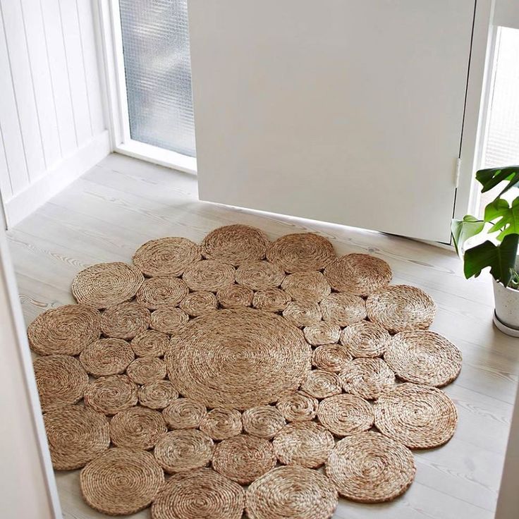 Round jute rug with circular pattern on light wooden floor, near a white door and a green potted plant. Cozy decor.