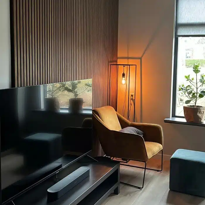 Modern living room with velvet chair, floor lamp, large TV, and window with plants. Cozy and stylish interior design.