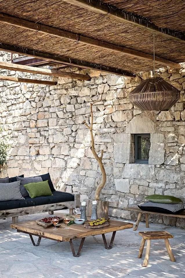 Rustic patio with stone walls, wooden furniture, and a straw ceiling, offering a cozy outdoor seating area.