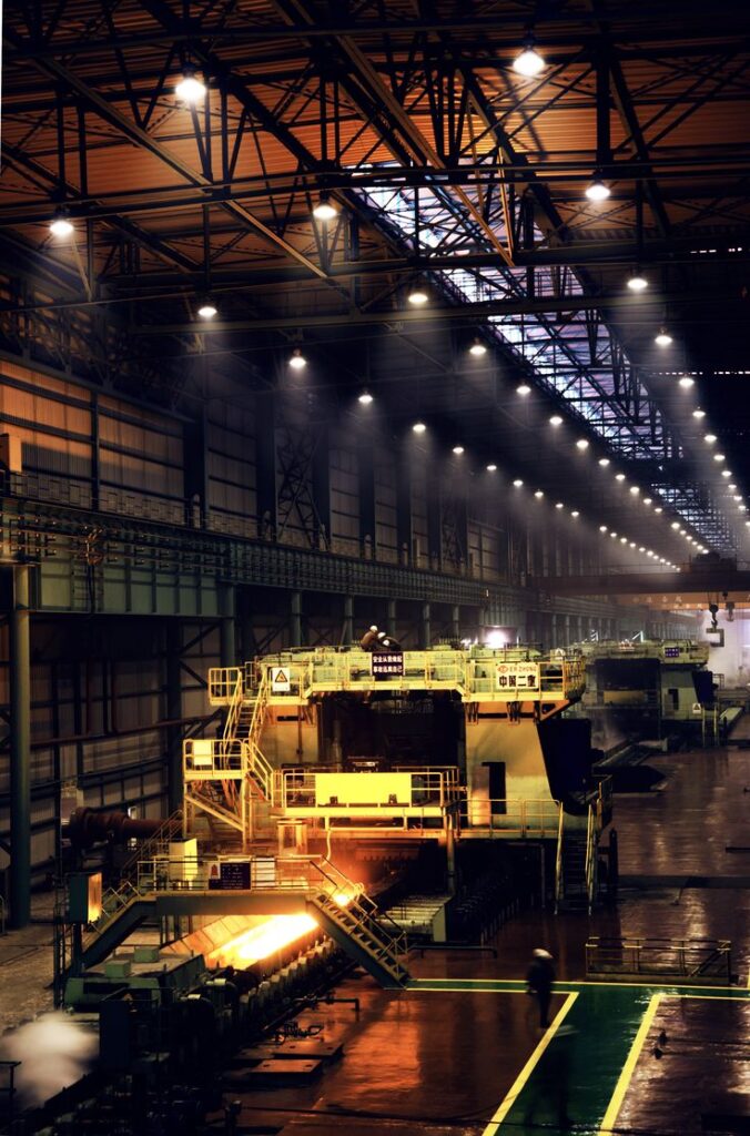 Interior view of a large industrial factory with machinery and illuminated ceiling lights.