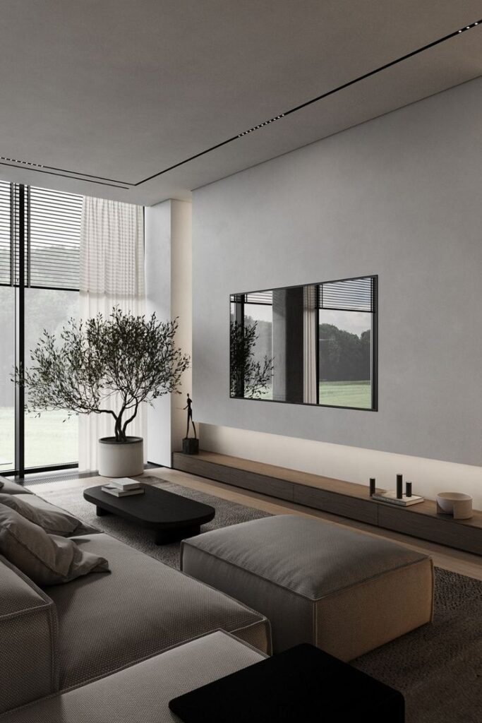 Minimalist living room with a large sofa, indoor plant, wall-mounted TV, and natural light through large windows.