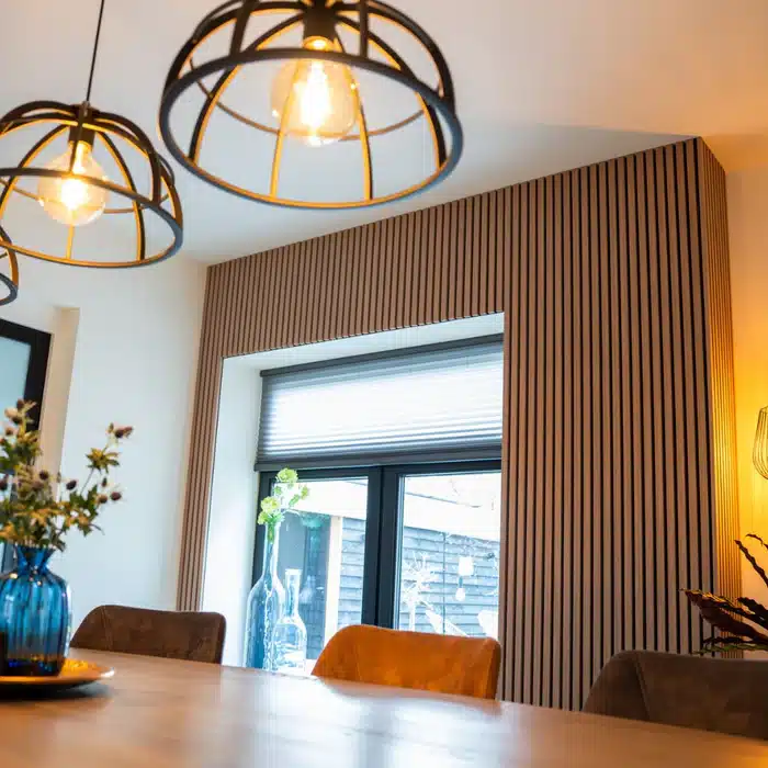 Modern dining area with stylish pendant lights, slatted wooden wall, and decorative plants near a sunlit window.