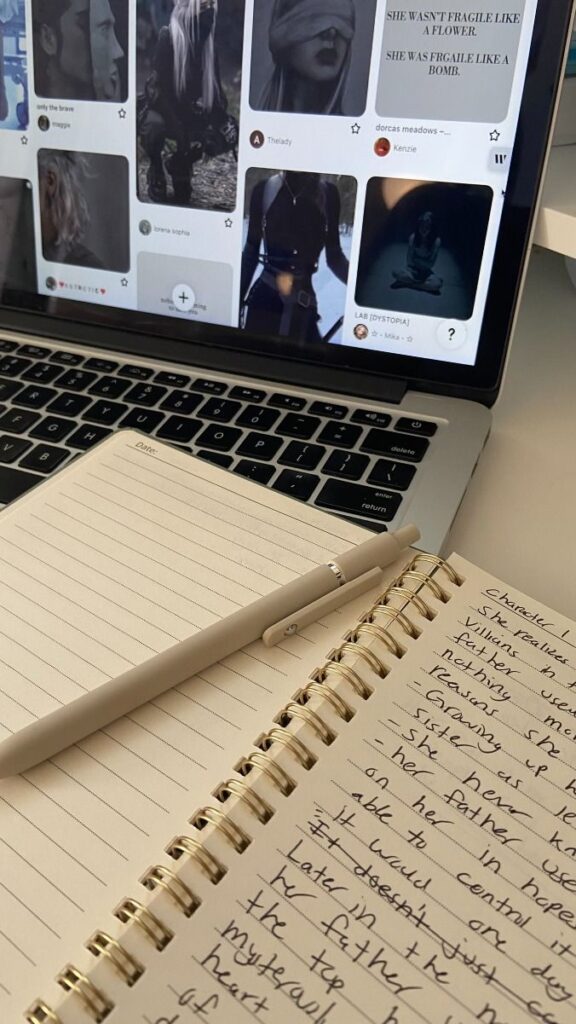 Open laptop displaying images, next to a notebook and pen with handwritten notes.