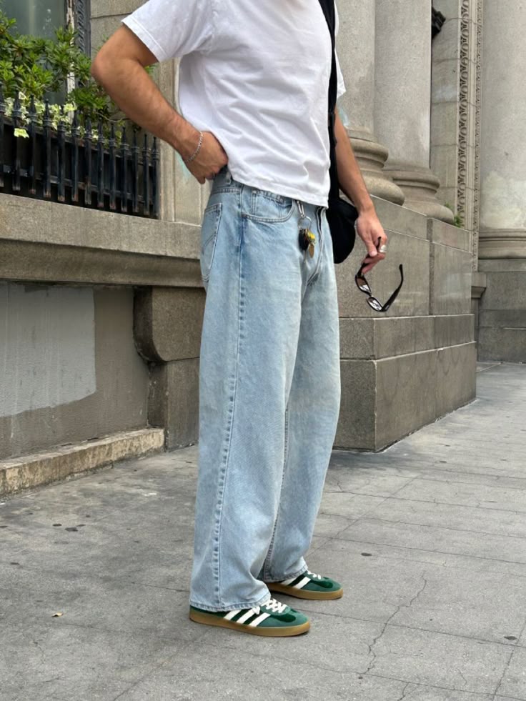 Man in casual white tee and baggy jeans stands on urban sidewalk.