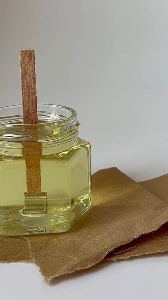 Glass jar with yellow wax and wooden wick on brown paper, ideal for DIY candles or home decor projects.