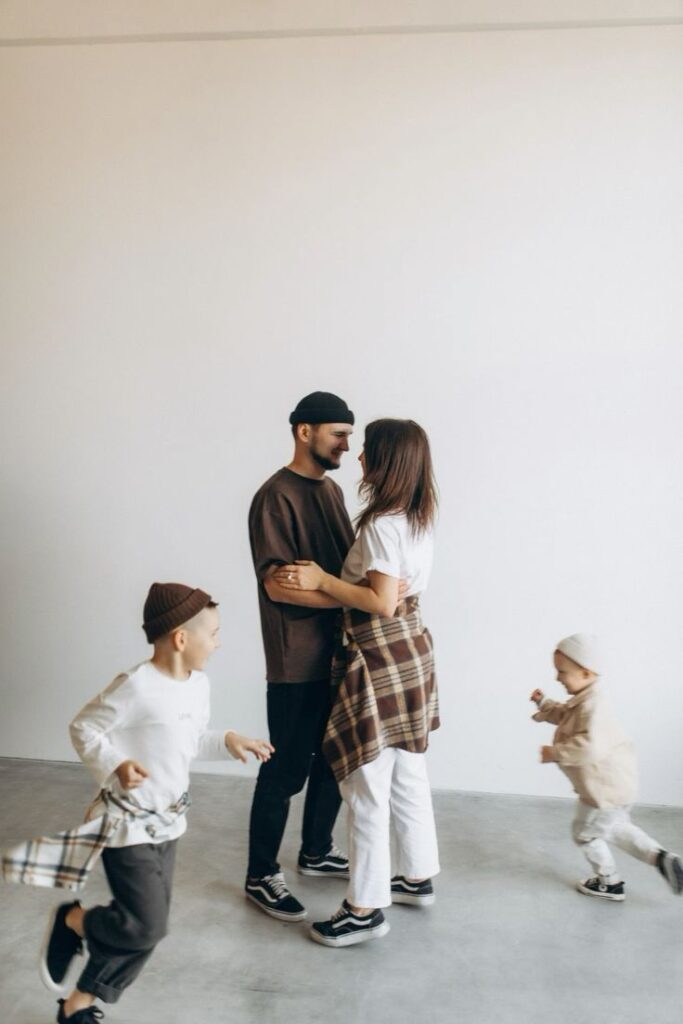 Happy family bonding, parents embracing, children playing around in a bright room.