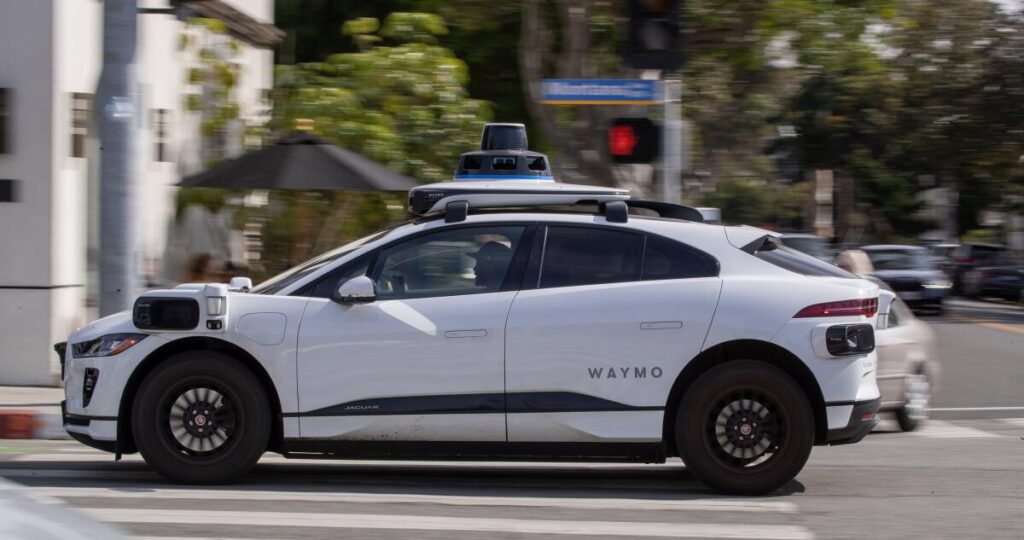 Autonomous Waymo vehicle driving on a city street, showcasing self-driving technology.