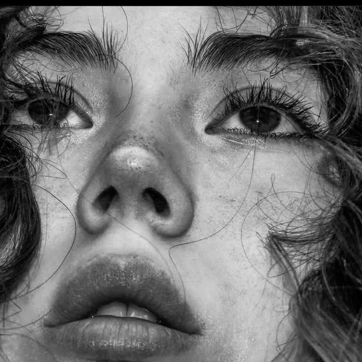 Close-up of a person's freckled face with curly hair, focusing on expressive eyes and natural beauty in black and white.