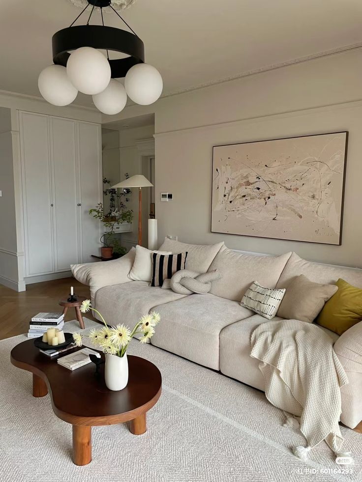 Modern living room with beige sofa, abstract art, chic lighting, and wooden coffee table with flowers for cozy ambiance.