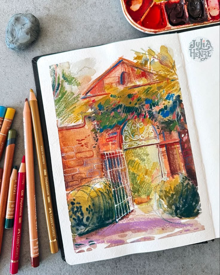 Colorful watercolor painting of a quaint house with an archway, surrounded by foliage, pencils and paints nearby.
