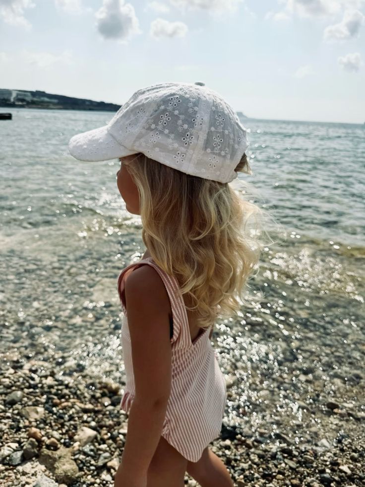 Young girl in striped swimsuit and white cap enjoying sunny beach by the sea.
