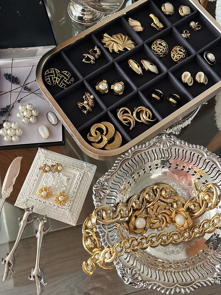 Винтажные украшения Collection of elegant vintage jewelry and accessories, including earrings, brooches, and gold chains on display trays. | Sky Rye Design Collection of elegant vintage jewelry and accessories, including earrings, brooches, and gold chains on display trays.