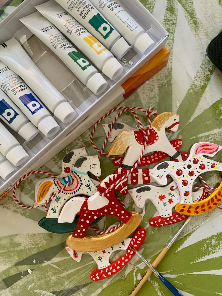 Елочные игрушки из полимерной глины_ Craft supplies and painted rocking horse ornaments with acrylic paints on a table. | Sky Rye Design Craft supplies and painted rocking horse ornaments with acrylic paints on a table.