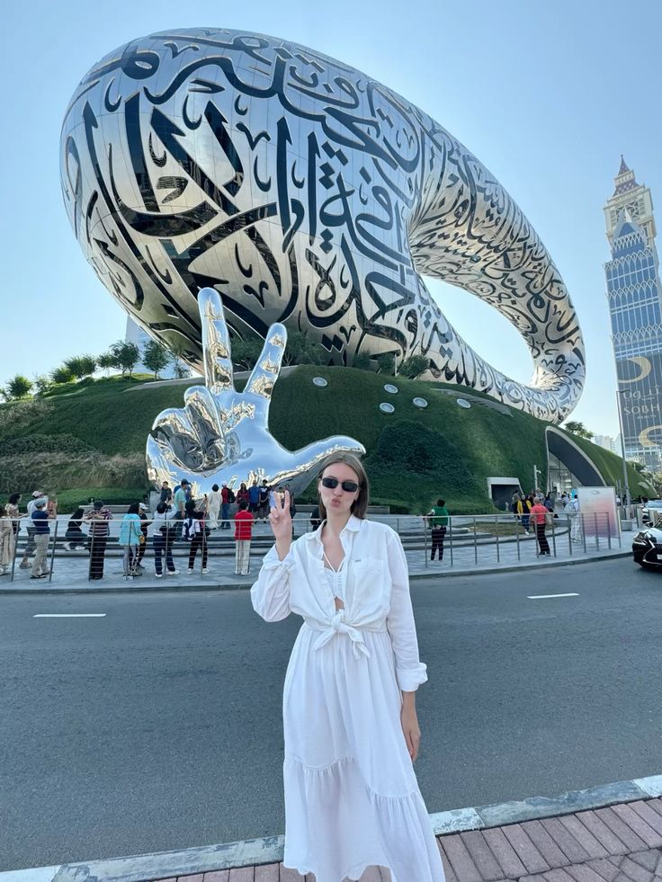Музей будущего Museum of the future Woman poses outside the Museum of the Future, Dubai, with large metal sculpture and Arabic calligraphy in the background. | Sky Rye Design Woman poses outside the Museum of the Future, Dubai, with large metal sculpture and Arabic calligraphy in the background.