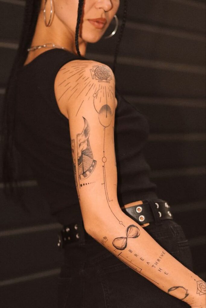 ТАТУ МОСКВА _ АЭЛИТА tattoo_aelita Instagram photos and videos Woman with arm tattoos, wearing a black top and hoop earrings, standing against a dark background. | Sky Rye Design Woman with arm tattoos, wearing a black top and hoop earrings, standing against a dark background.