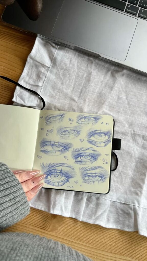 блог художника 🍵 цифровой художник арт скетч рисование _ дизайн историй Sketchbook with multiple eye drawings on a table next to a laptop, showcasing artistic creativity. | Sky Rye Design Sketchbook with multiple eye drawings on a table next to a laptop, showcasing artistic creativity.
