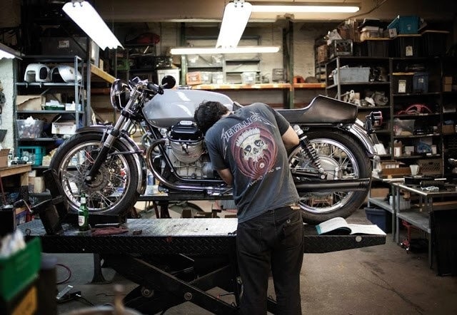 завантаження Mechanic working on a classic motorcycle in a workshop, surrounded by tools and equipment. | Sky Rye Design Mechanic working on a classic motorcycle in a workshop, surrounded by tools and equipment.