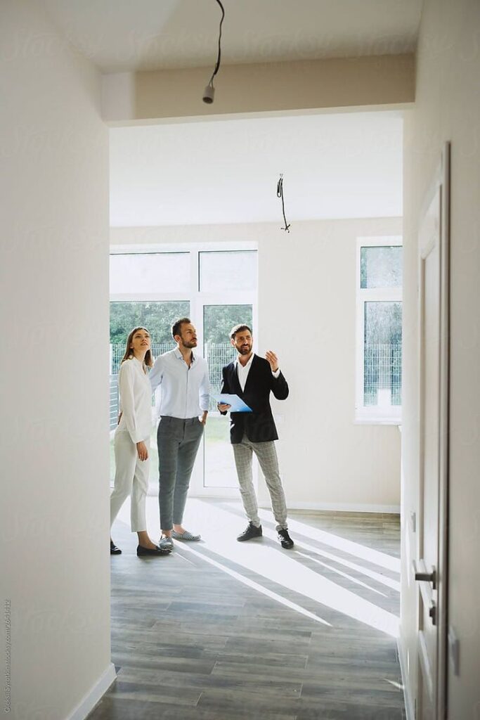 тут про бизнес Real estate agent showing couple a bright new home interior with large windows and wooden flooring. | Sky Rye Design Real estate agent showing couple a bright new home interior with large windows and wooden flooring.