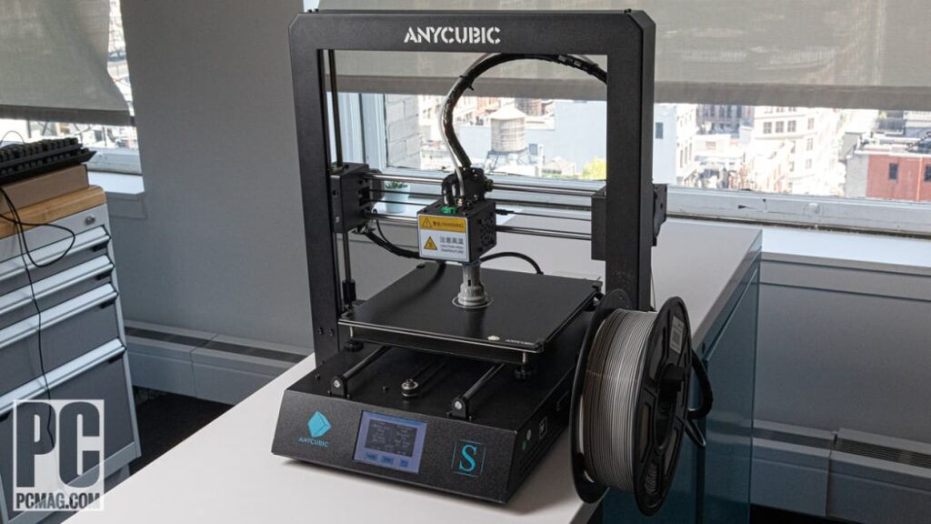 Anycubic 3D printer on a desk by a window, equipped with filament spool, ready for printing.