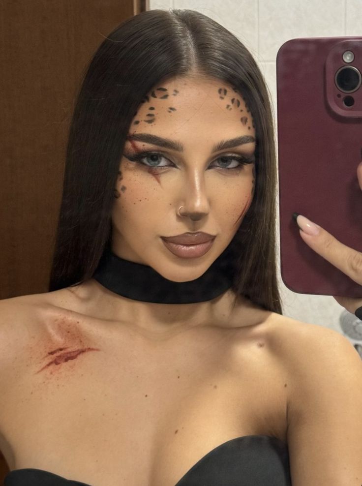 Woman with leopard-inspired makeup takes a selfie, wearing a black top and choker, showcasing artful face design.