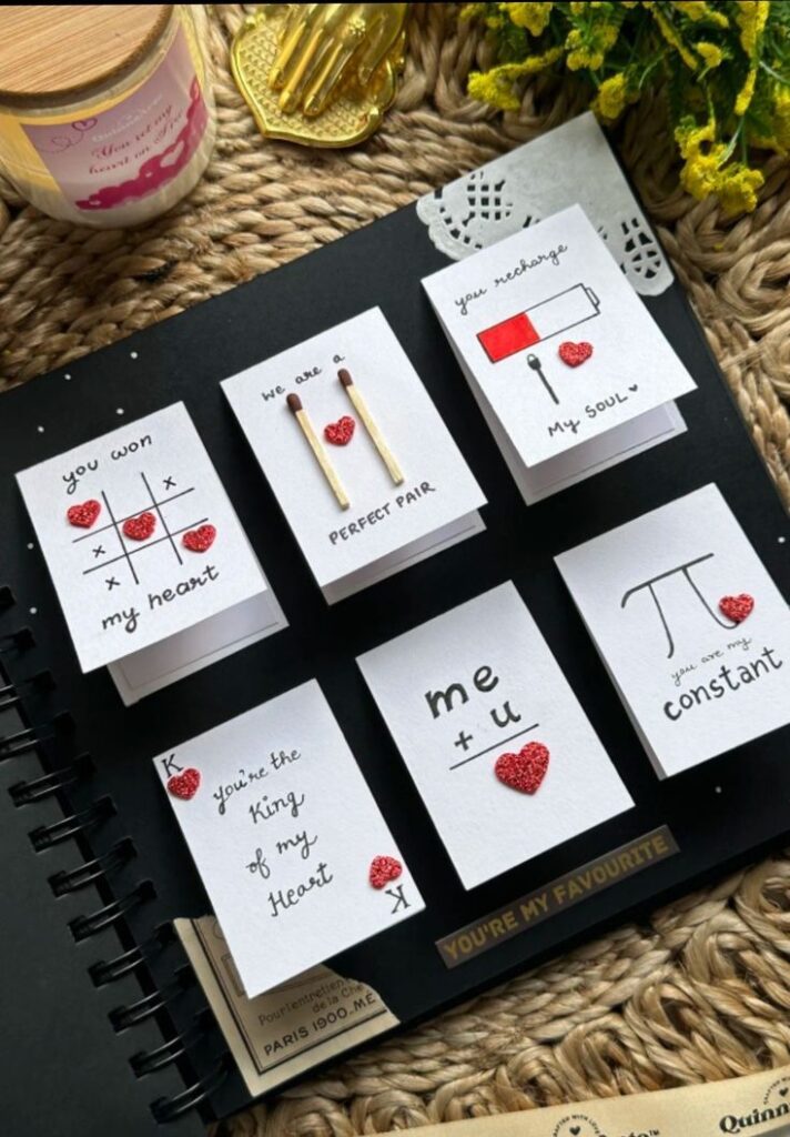 Romantic handmade cards with heart motifs on a black scrapbook, surrounded by a candle and flowers.