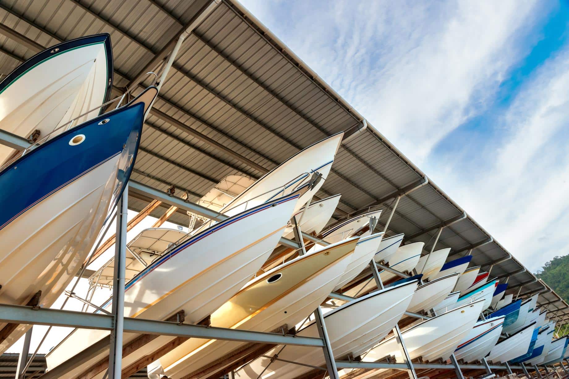 050439103-power-boats-sheltered-parking- Boats stored under covered dock on sunny day with blue sky, highlighting marina storage solutions. | Sky Rye Design Boats stored under covered dock on sunny day with blue sky, highlighting marina storage solutions.