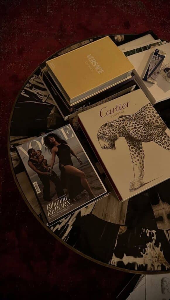 Fashion magazines on black marble table: Vogue cover, Versace hardcover, and Cartier book with a leopard design.
