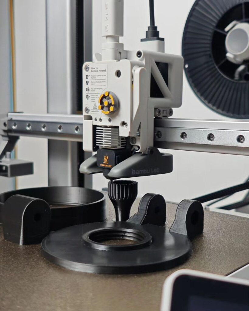 3D printer in action, focusing on hotend and extruder details, with a filament spool in the background.