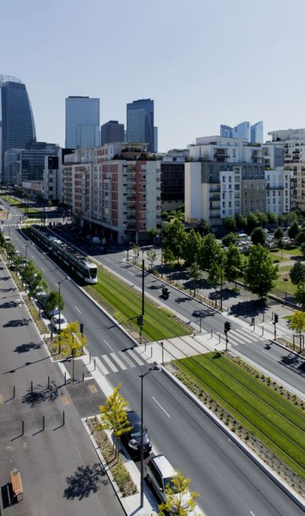 A modern cityscape with skyscrapers, a tram on tracks, and tree-lined streets on a sunny day.