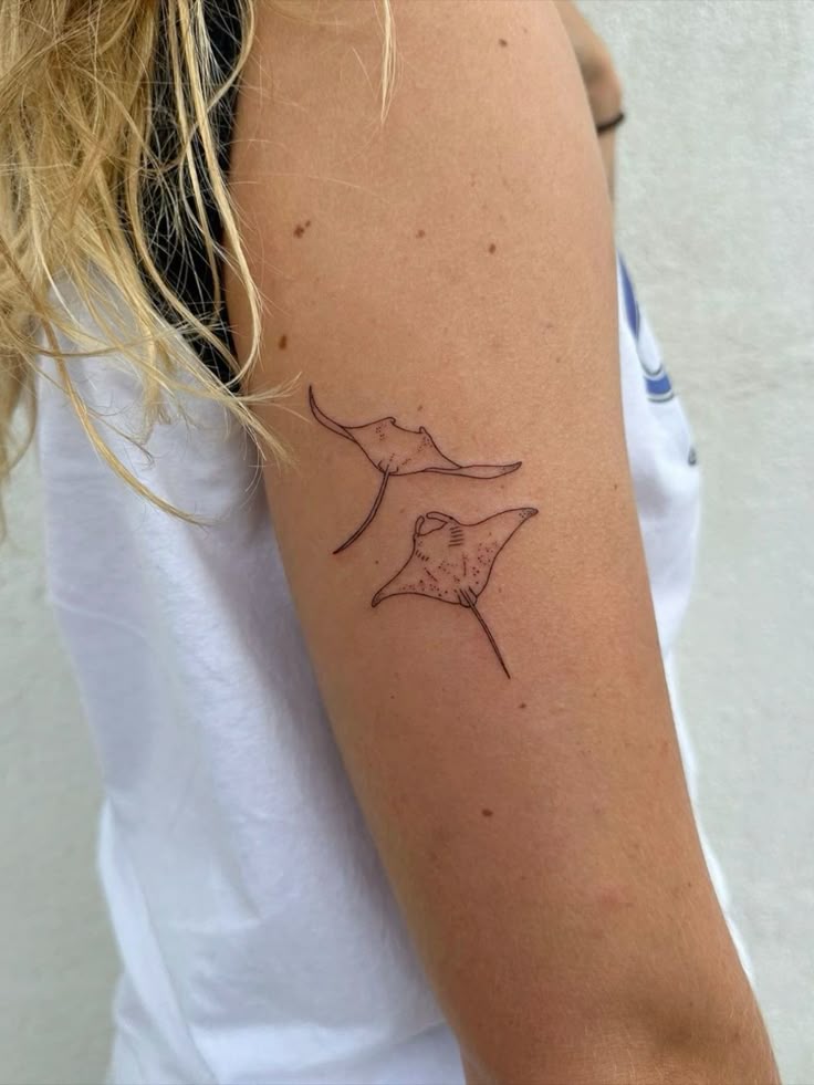 Two manta ray tattoos on a person's upper arm, minimalist black ink design.