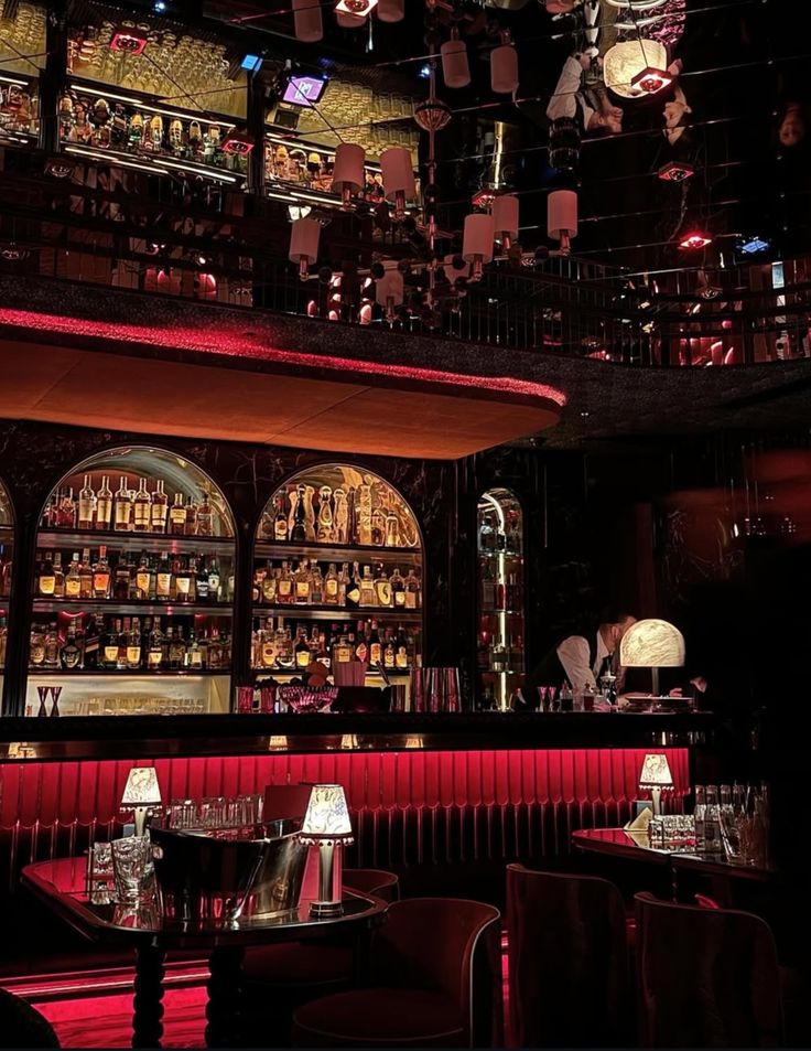 Luxurious dimly lit bar interior with red accents, shelves of liquor bottles, and elegant table settings.