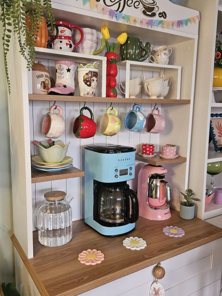 Colorful coffee station with vintage mugs, a blue coffee maker, and a pink kettle on wooden shelves.