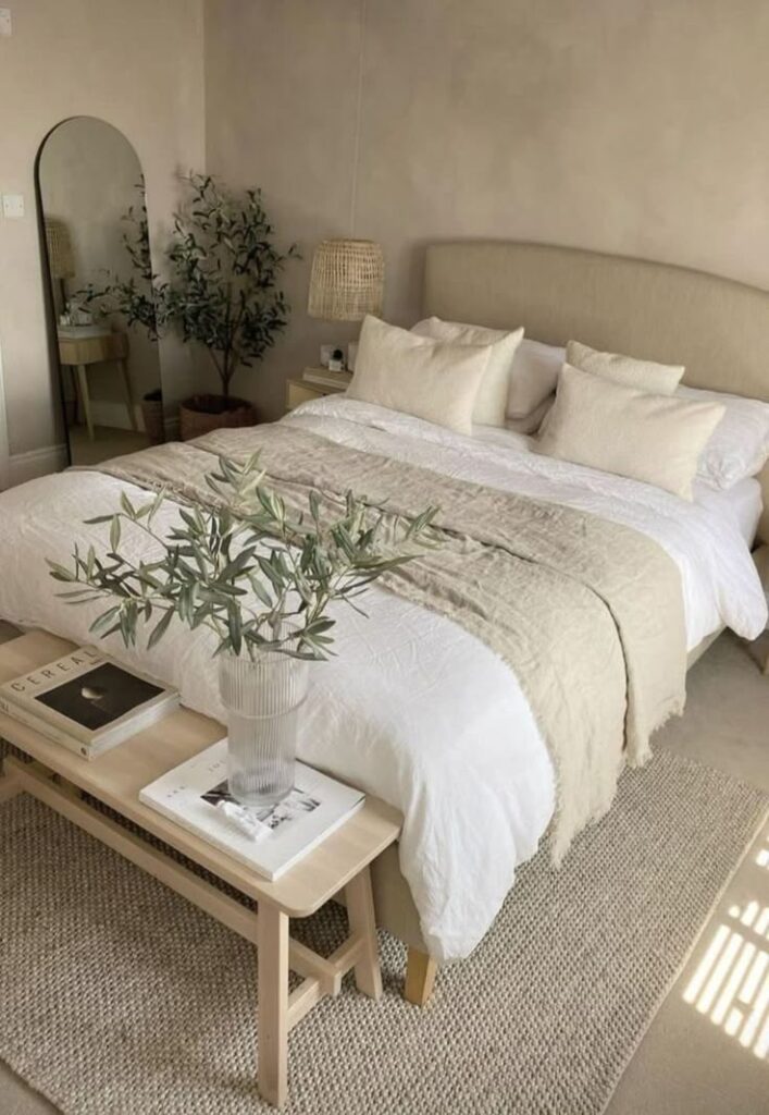 Minimalist bedroom with beige bedding, green plant, and wooden bench enhances cozy, modern interior design.
