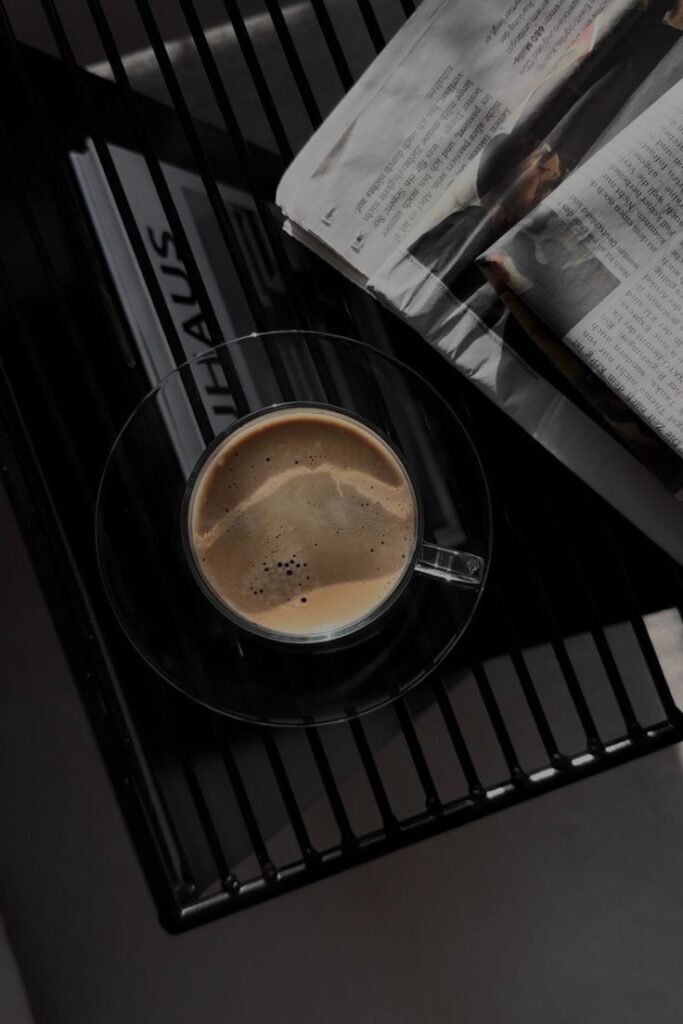 Cup of coffee and newspaper on black table, creating a cozy reading vibe.