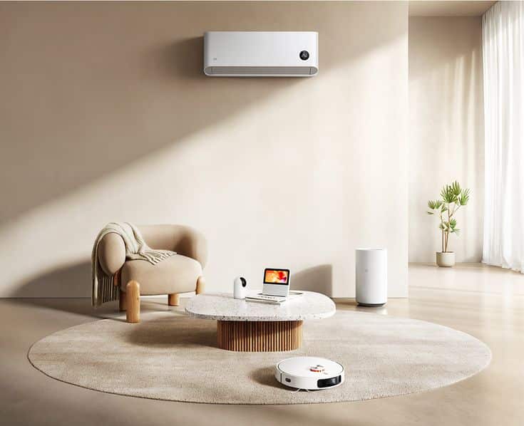 Modern living room with smart home devices, including a laptop, air purifier, and robotic vacuum on a beige carpet.