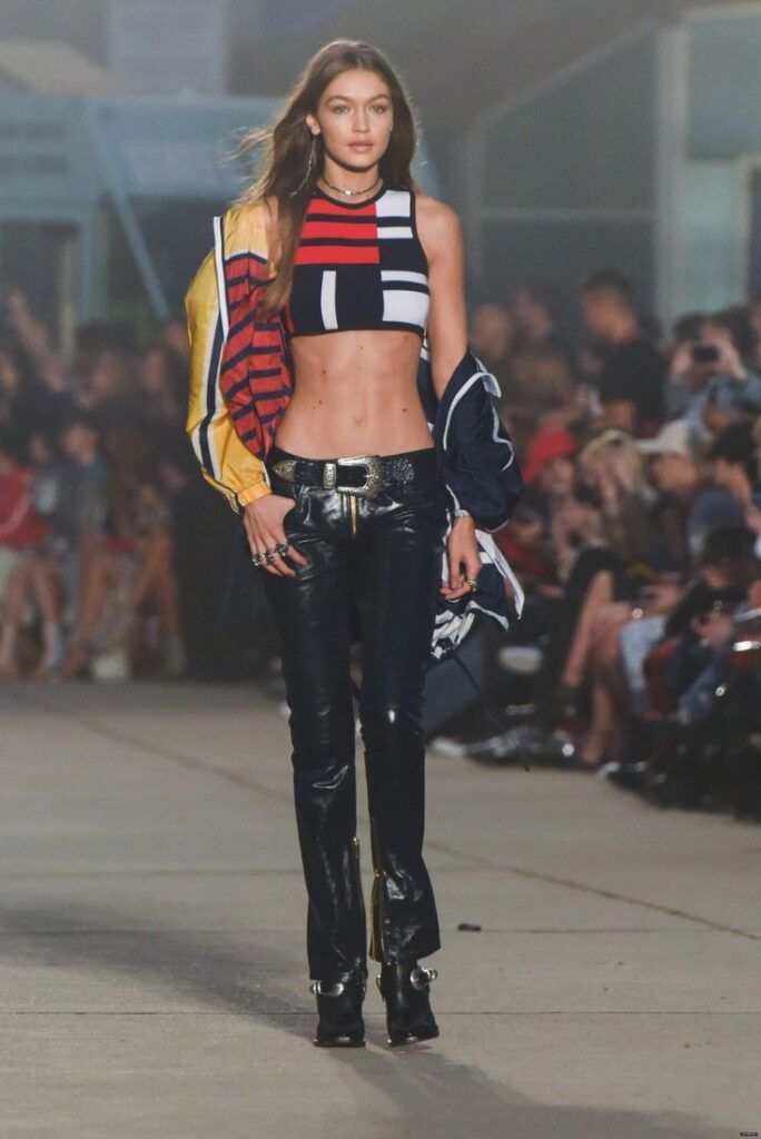 Model walking runway in a colorful crop top and leather pants at a fashion show.