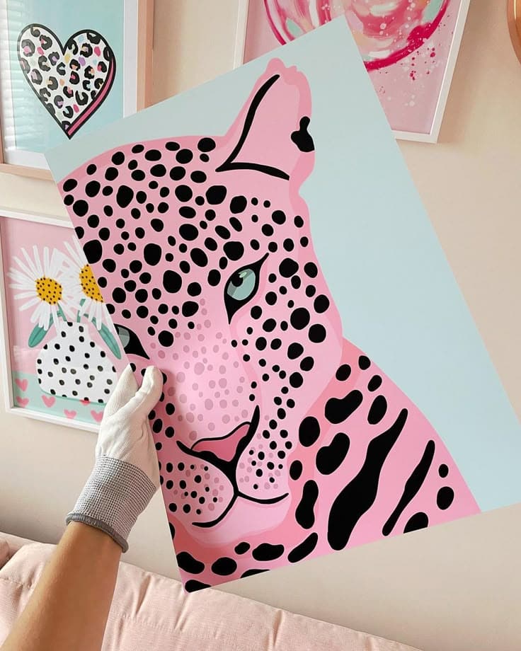 Person holding a pastel pink leopard artwork with dotted patterns, surrounded by colorful frames.